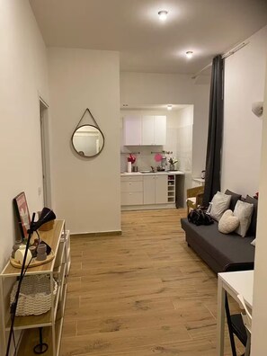 A modern apartment with a wooden floor, a dark sofa, a small table, and a kitchen in the background. - Bocca di rosa in centro (La Spezia)