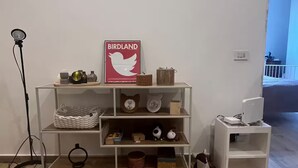 A room with a wooden floor, a white wall, a shelf with various items, and a poster. - Bocca di rosa in centro (La Spezia)