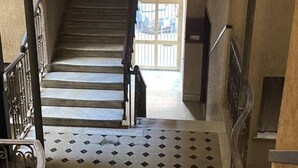 A staircase with a patterned floor and metal railings, leading to a bright area with a window. - Bocca di rosa in centro (La Spezia)