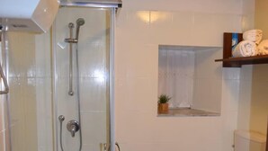Un bany amb dutxa de vidre, un vàter i una estant amb tovalloles.