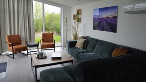 Ein modernes Wohnzimmer mit einem grünen Sofa, zwei Sesseln, einem Couchtisch und einem großen Fenster mit Vorhängen.
