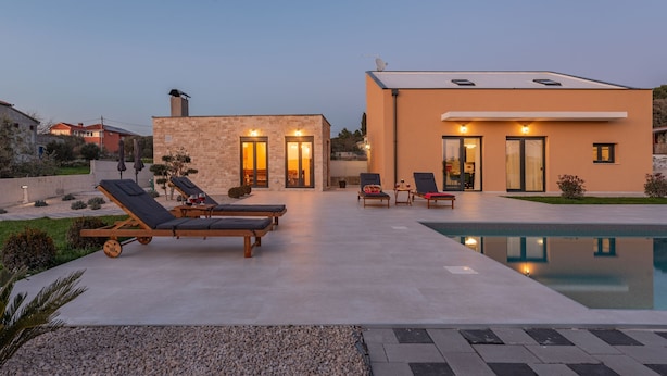 A modern house with a swimming pool, lounge chairs, and a well-maintained garden.