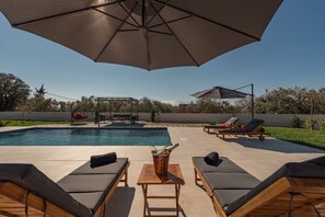 An outdoor pool area with lounge chairs, a wooden table with a bottle, and umbrellas. - Villa Dide Moga Zadarvillas (Sveti Filip i Jakov)
