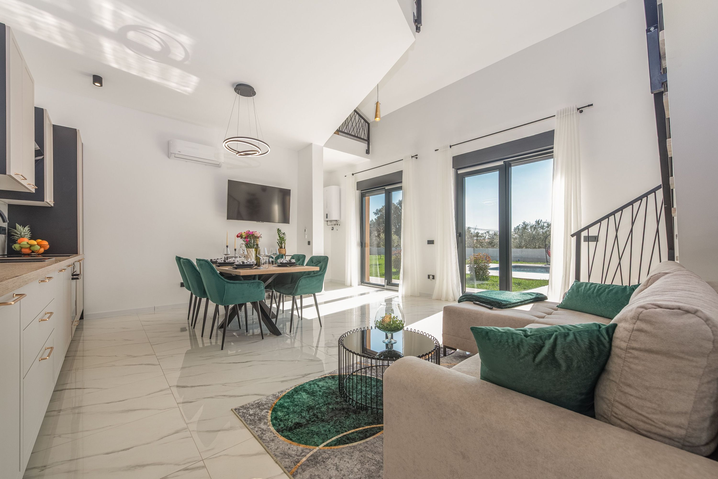 A modern living room with a sofa, a dining area with chairs, a kitchen with a counter, and a large window.