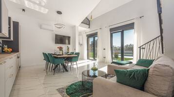 A modern living room with a sofa, a dining area with chairs, a kitchen with a counter, and a large window.