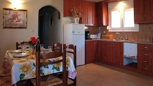 Zona pranzo con tavolo apparecchiato per quattro persone, frigorifero, pensili in legno e finestra che lascia entrare luce naturale.