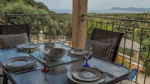 Un tavolo apparecchiato per due su un balcone con vista su un paesaggio pittoresco, colline e uno specchio d'acqua in lontananza.