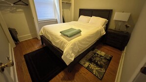 Un dormitorio con cama, mesita de noche, lámpara y una ventana con persianas.