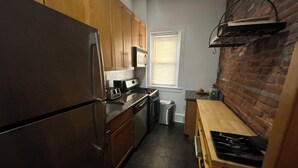 Cocina compacta con armarios de madera, refrigerador de acero inoxidable, microondas, tostadora y un lavamanos pequeño.