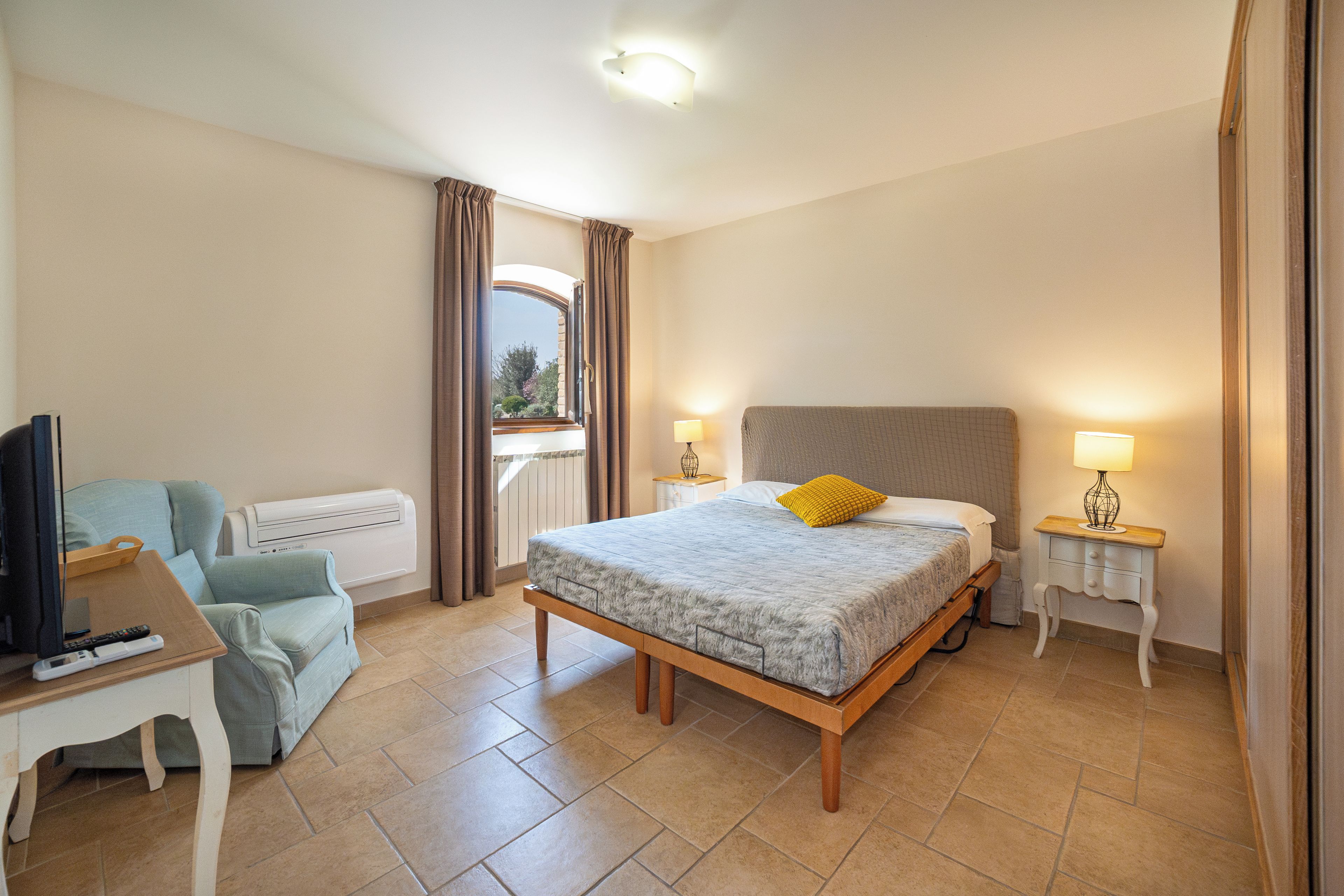 Une chambre à coucher avec un lit, un bureau et une chaise, une télévision et une fenêtre avec des rideaux.
