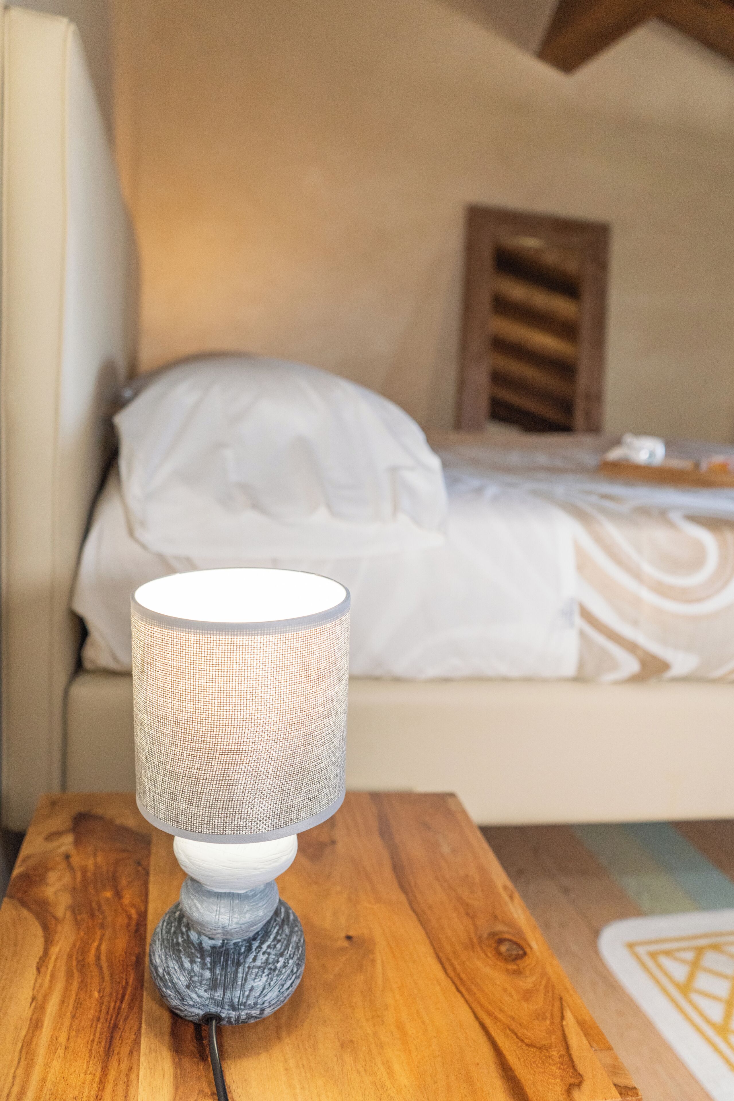 A lamp on a wooden table in a room with a bed and a window.