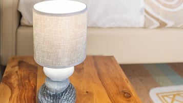 A lamp on a wooden table in a room with a bed and a window.