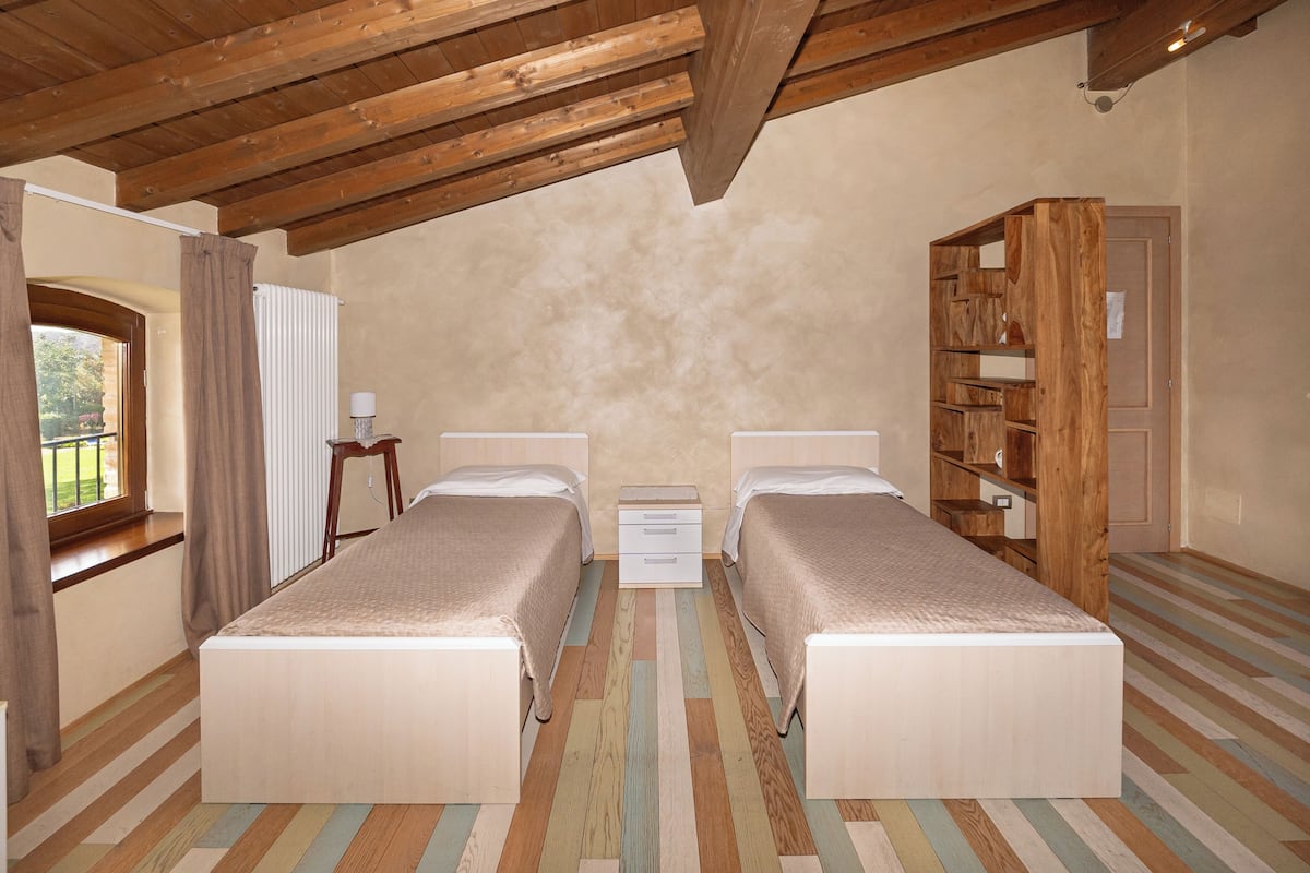 Un dormitorio con dos camas, techo de madera, ventana con cortinas y una estantería de madera.