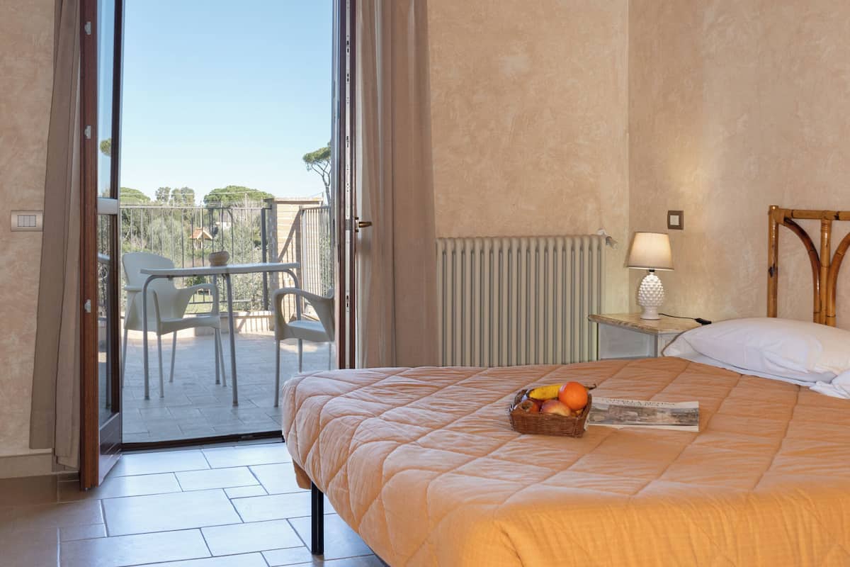 Un dormitorio con cama, mesita de noche, lámpara, ventana con cortinas y vistas al exterior.