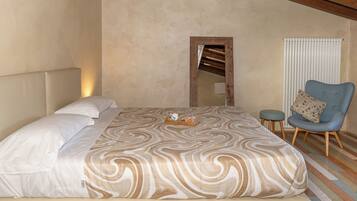 A bedroom with a large bed, a chair, a small stool, a radiator, and a mirror on the wall.