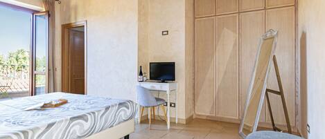 A bedroom with a bed, a desk with a computer, a wardrobe, and a balcony.