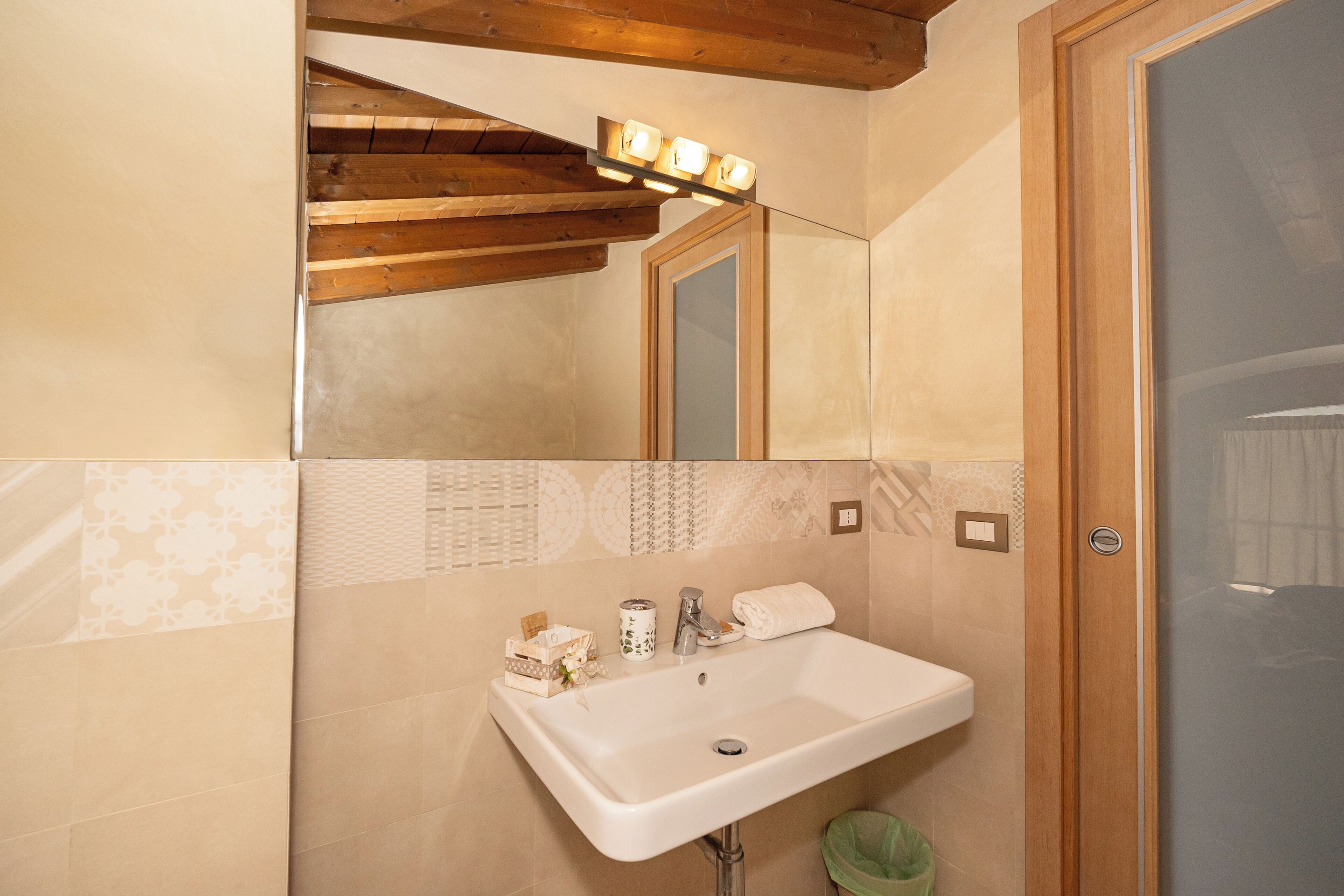 A bathroom with a sink, mirror, vanity lights, and a trash bin.