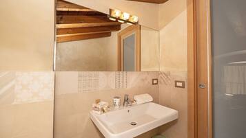 A bathroom with a sink, mirror, vanity lights, and a trash bin.