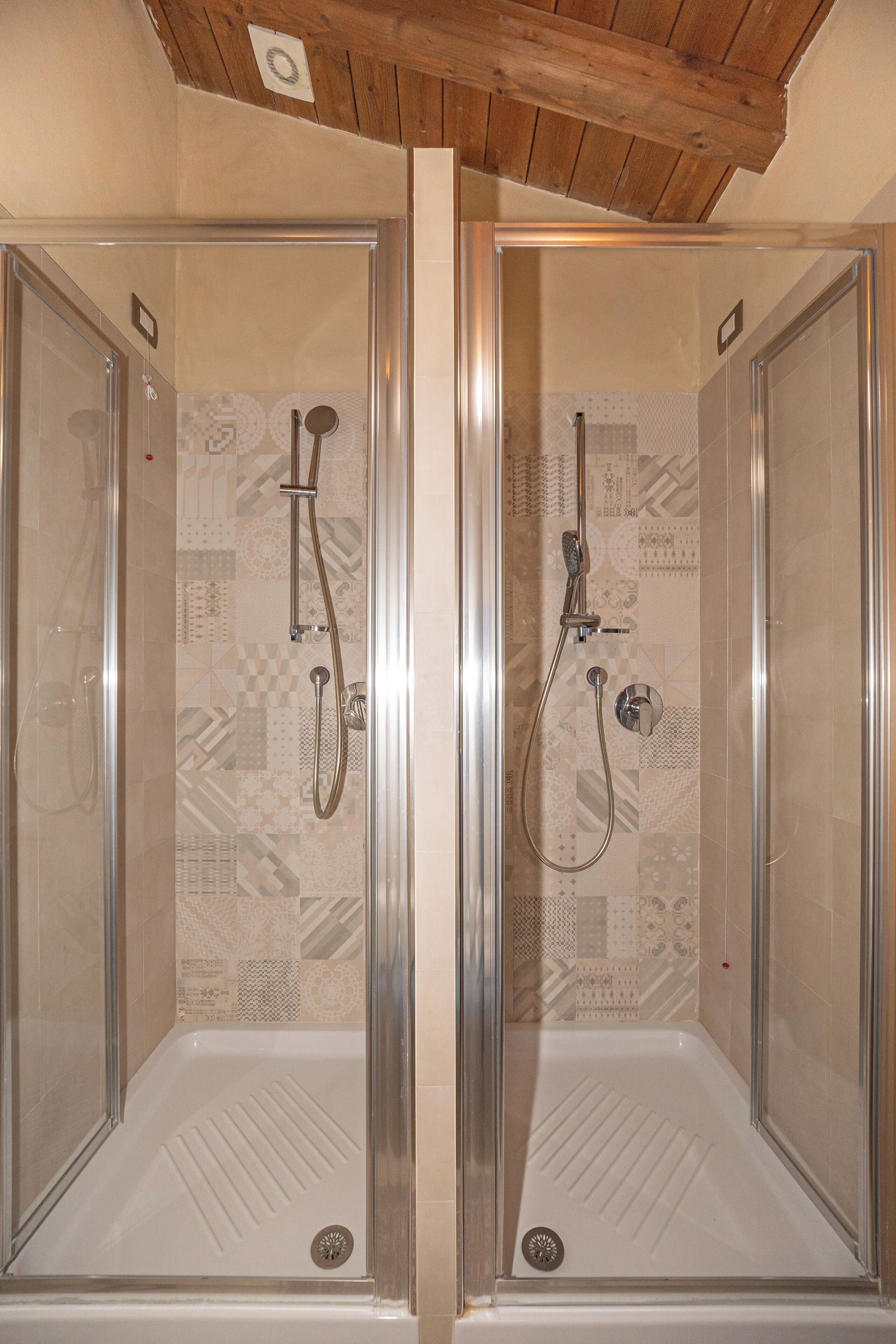 A mirrored bathroom with a shower enclosure, tiled walls, and a wooden ceiling.