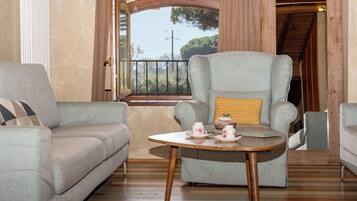 Une pièce comprenant un canapé, un fauteuil, une table avec des tasses à thé et une fenêtre donnant sur des arbres.