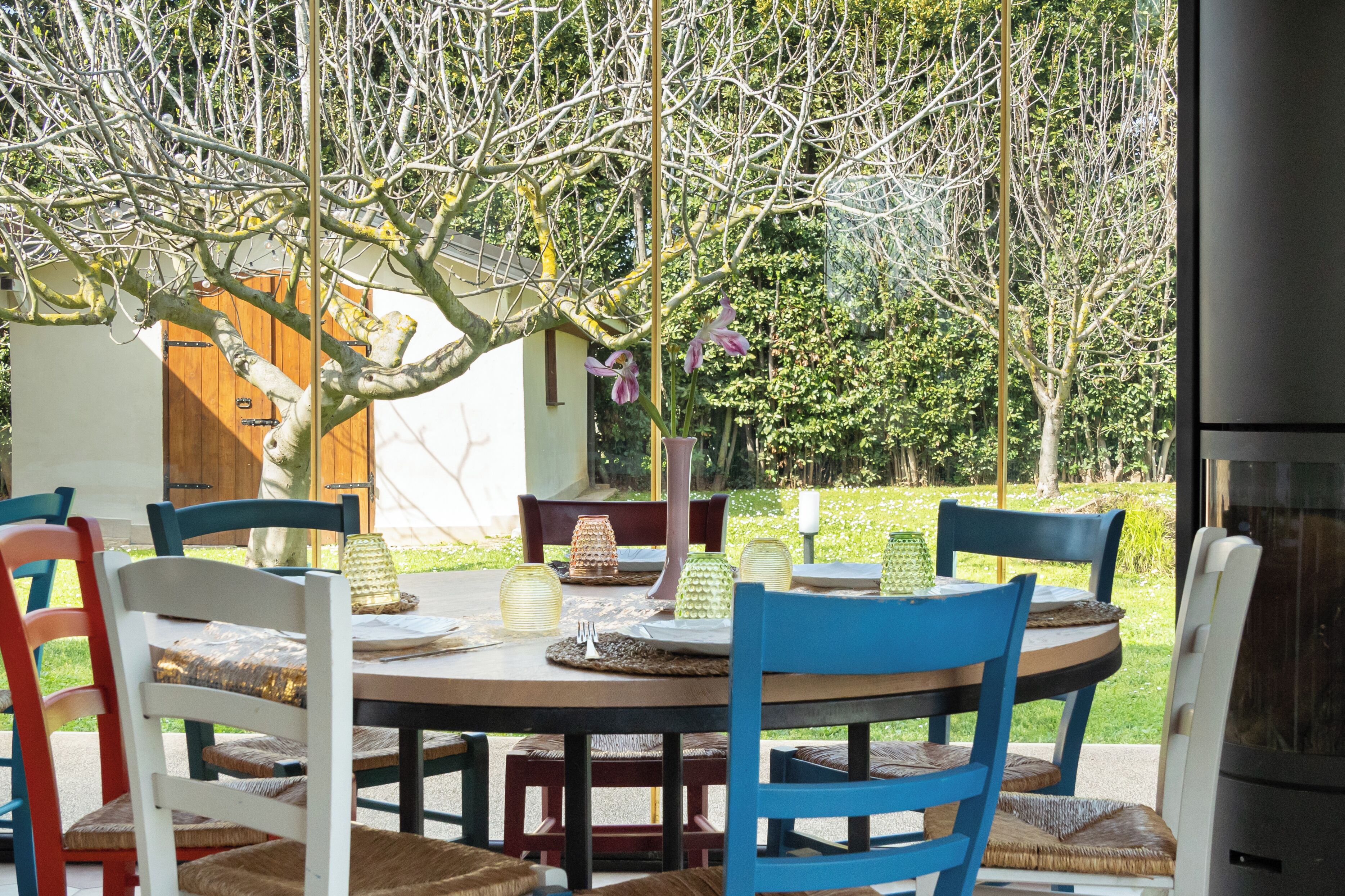 Een terras met een ronde tafel, stoelen en uitzicht op een tuin.