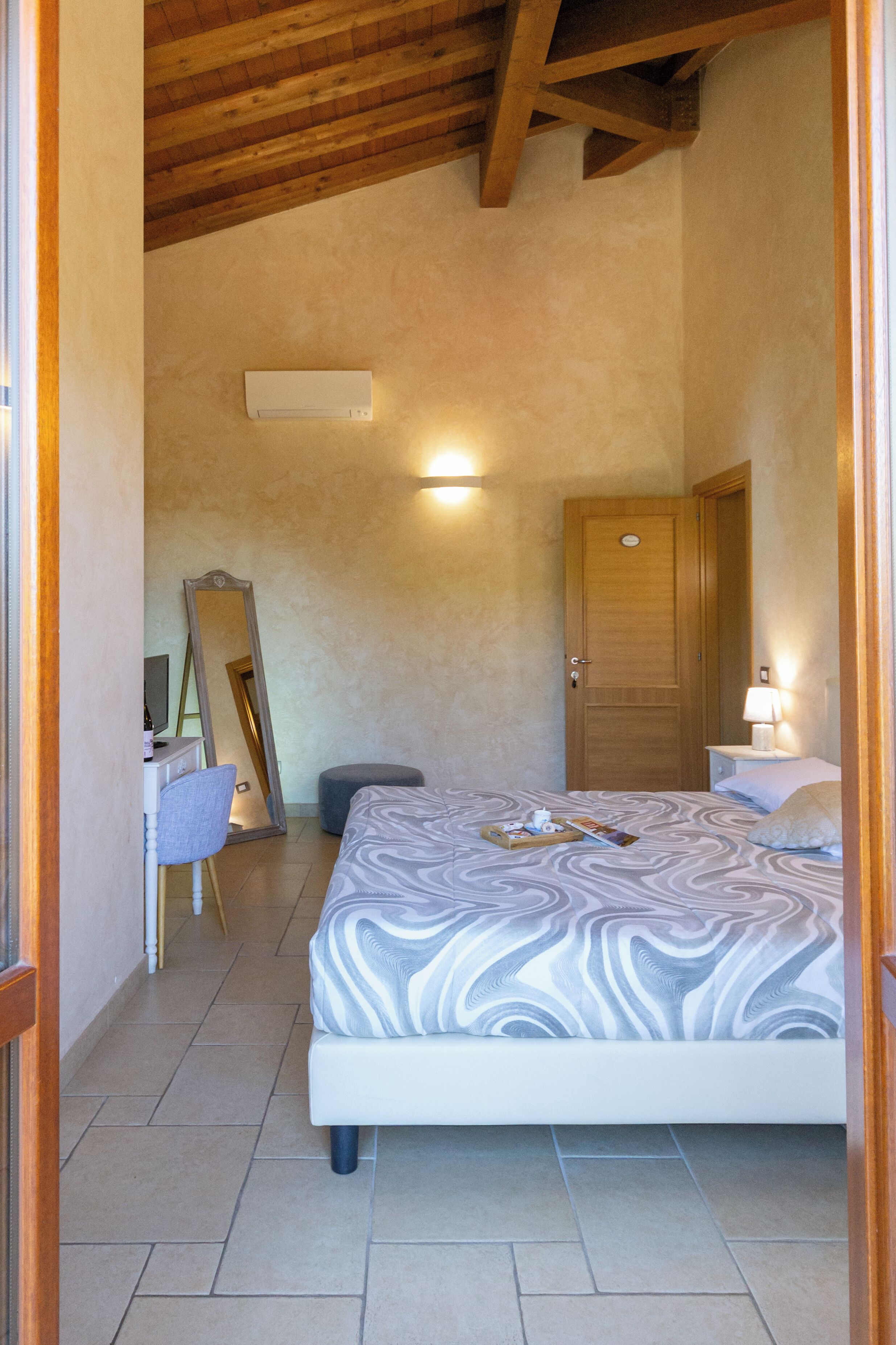 A bedroom with a bed, a dresser, a mirror, a door, and a nightstand with a lamp.