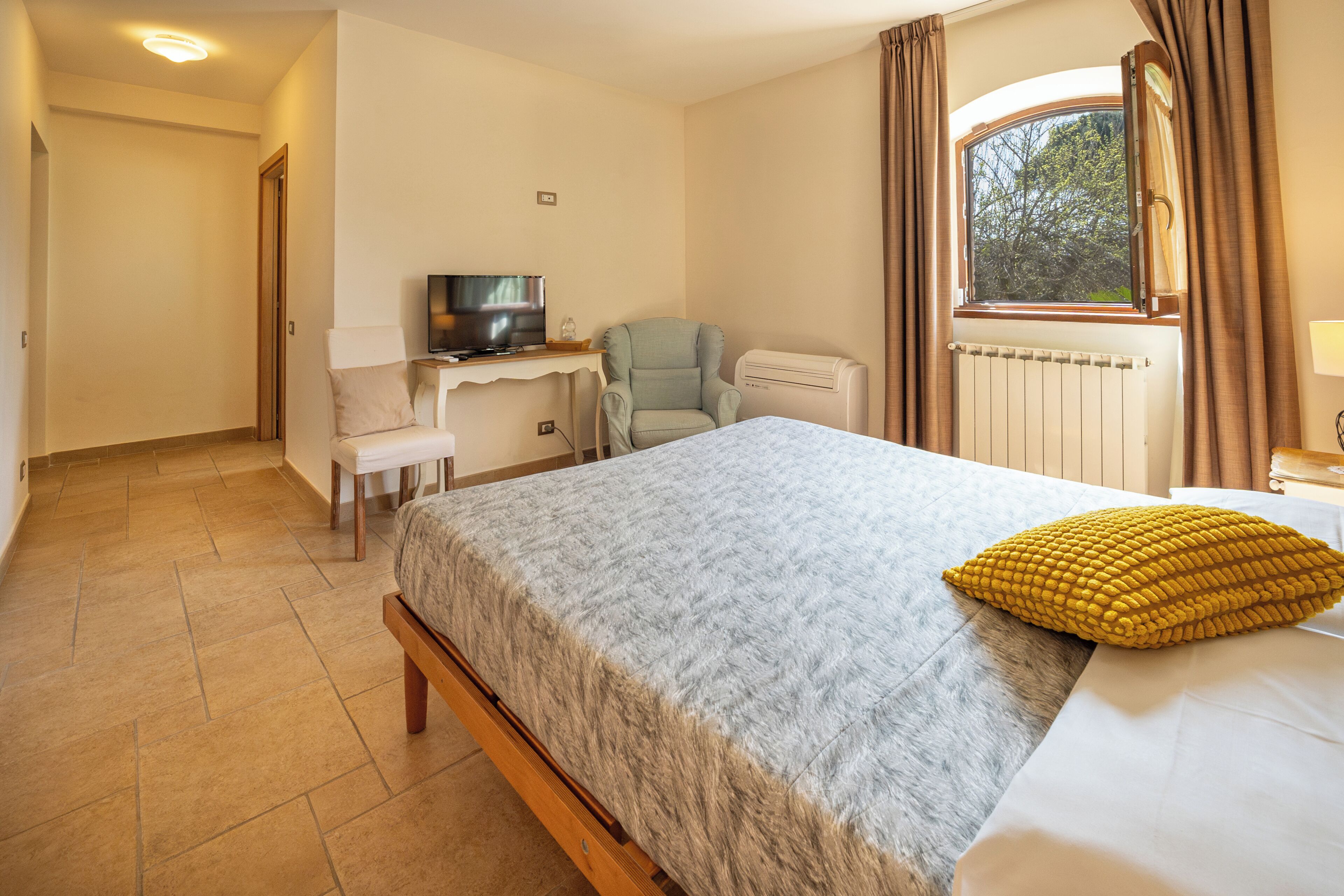 Een hotelkamer met een bed, een bureau met een televisie, een stoel en een raam met gordijnen.
