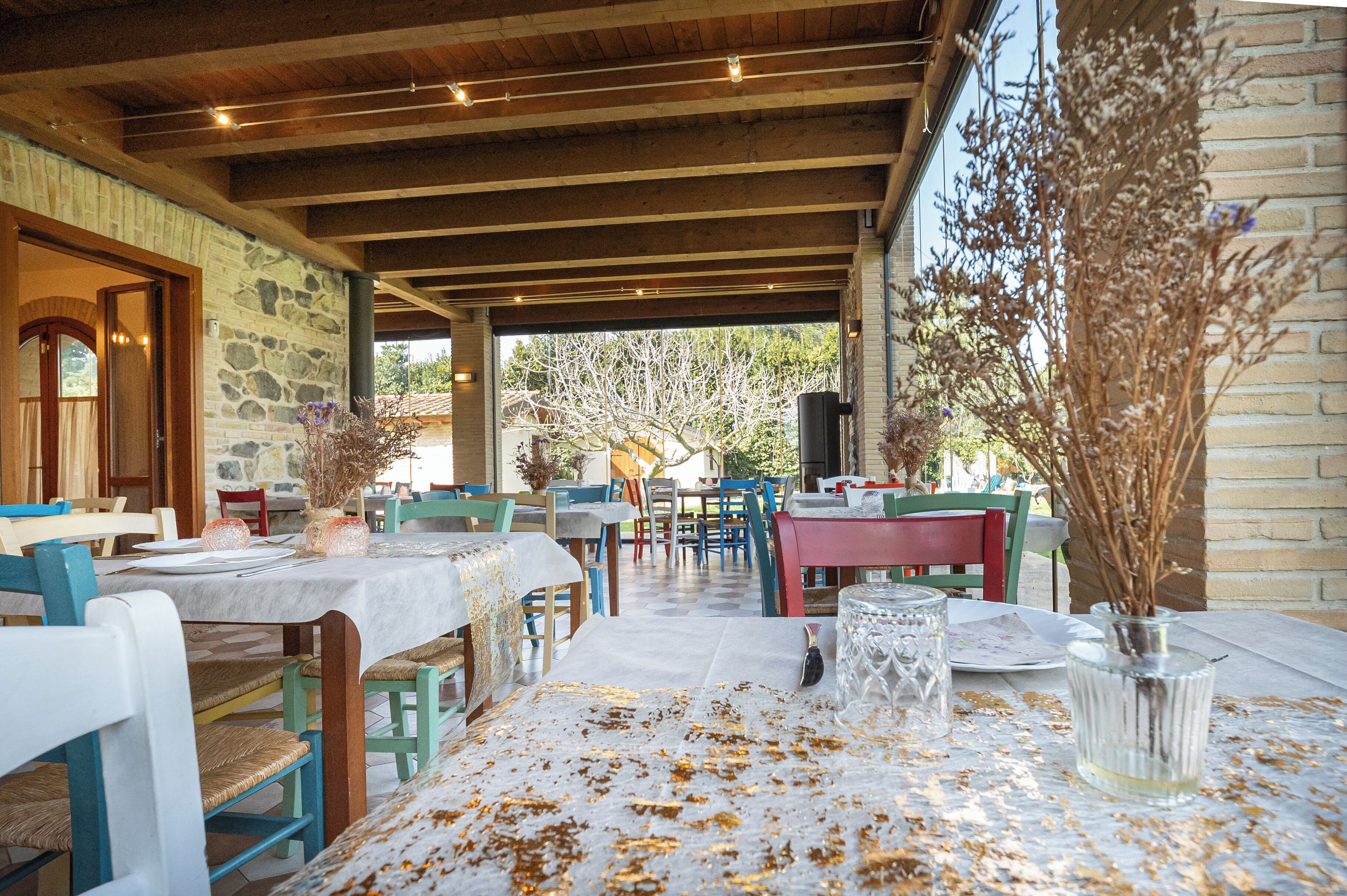 An outdoor dining area with stone walls, wooden beams, and tables set for dining.