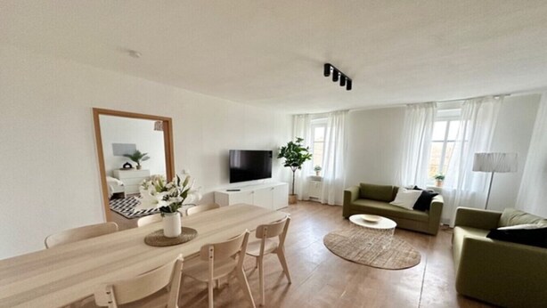 A modern living room with a wooden dining table, a sofa, and a TV. - Arbio Monteurzimmer Tremmen 6 people (Ketzin)