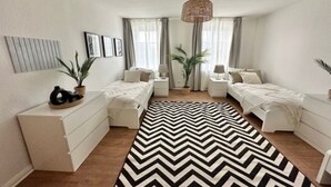 A modern bedroom with two beds, a black and white chevron rug, and a hanging light fixture. - Arbio Monteurzimmer Tremmen 6 people (Ketzin)