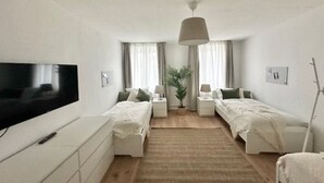 A modern bedroom with two beds, a TV, a plant, and a bedside table with a lamp.