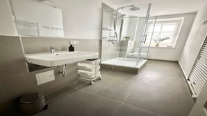 A modern bathroom with a glass-enclosed shower, a sink with a mirror, and a small window.