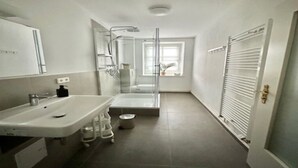 A narrow bathroom with a glass shower enclosure, a sink, and a toilet.