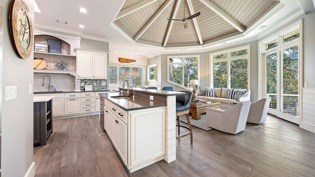 A spacious kitchen with a central island, a dining area with a sofa and chairs, and large windows offering views of the outdoors. - 3 Brigantine - Incredible 2nd Row Home in Palmetto Dunes (Hilton Head Island)