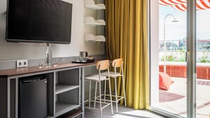 A modern hotel room with a flat-screen TV, a small kitchenette, a bar area with two stools, and a large window with a yellow curtain. - BYPILLOW Flamant (Barcelona)