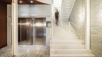 Un interior moderno con una escalera, un ascensor de acero inoxidable y una pared de ladrillo.