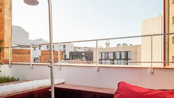 Una terraza en la azotea con ducha moderna, cojines rojos y un toldo a rayas.