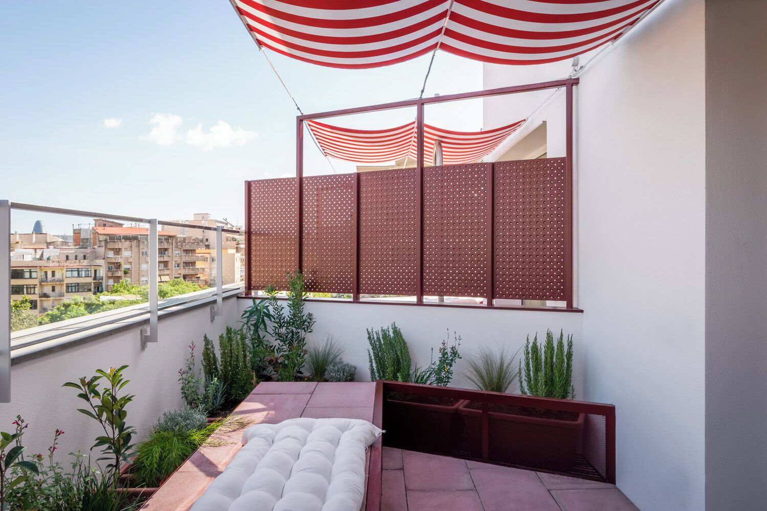 Un balcón con zona de estar acolchada, vistas de la ciudad y un toldo blanco y rojo a rayas.