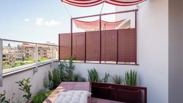 Un balcón con zona de estar acolchada, vistas de la ciudad y un toldo blanco y rojo a rayas.