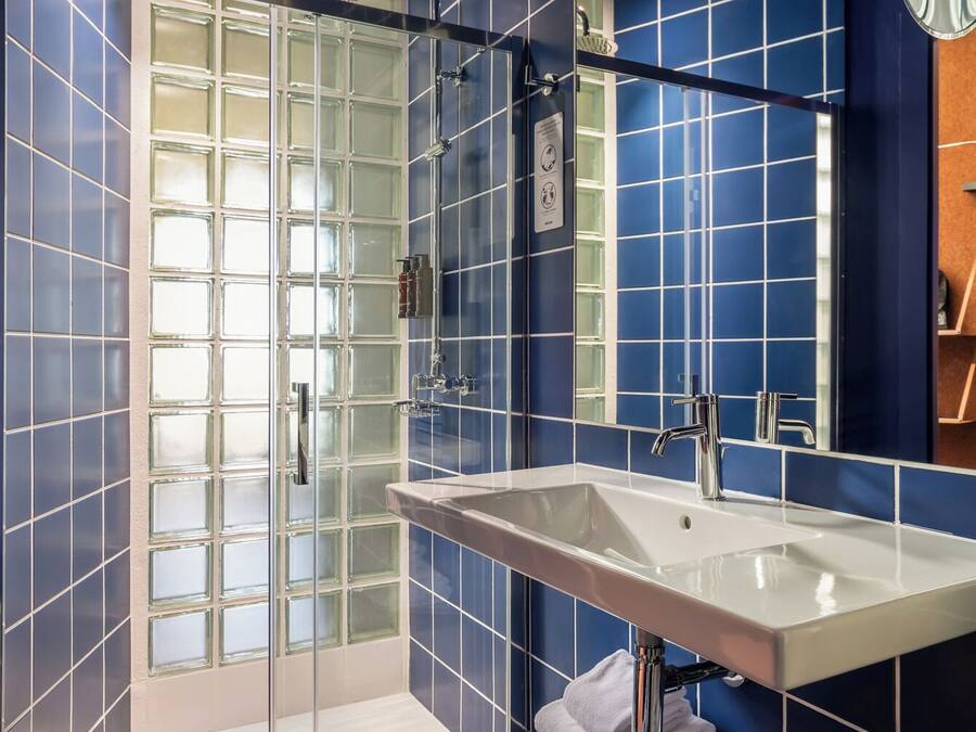 Un baño con cabina de ducha de vidrio, un lavabo blanco y un espejo grande.