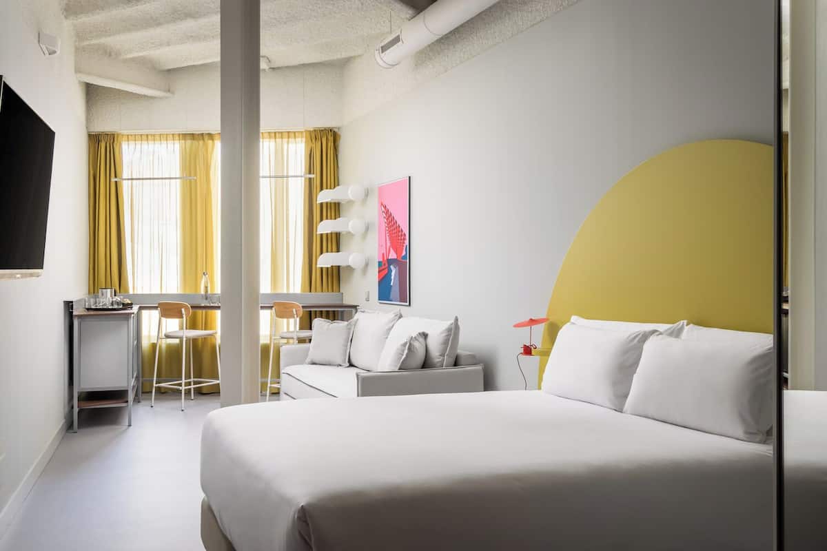 Une chambre d’hôtel moderne, dotée d’un grand lit, d’un bureau avec une chaise, d’un canapé et d’un téléviseur fixé au mur.