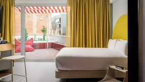 A modern hotel room with a large bed, a desk, and a view of an outdoor patio with a red and white striped awning. - BYPILLOW Flamant (Barcelona)