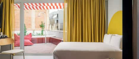 Una habitación de hotel moderna con una cama grande, un escritorio y vistas a un patio exterior con un toldo a rayas rojas y blancas.