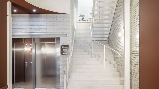 A modern interior with a staircase leading to an upper level, a reception area with a sign, and a patterned floor. - BYPILLOW Flamant (Barcelona)