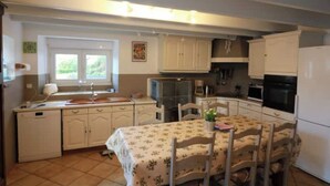 A compact kitchen with white cabinets, a dining table with a floral tablecloth, and a refrigerator. - beach 250 meters,large park,wifi, bicycles provided, large terrace for breakfast (Audierne)