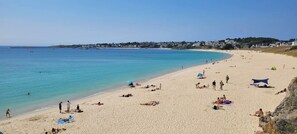 A wide sandy beach with clear blue water, a few umbrellas, and people relaxing.
