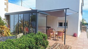 A glass-enclosed patio with a table and chairs, surrounded by greenery and a white building. - beach 250 meters,large park,wifi, bicycles provided, large terrace for breakfast (Audierne)