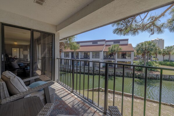 A balcony with wicker furniture, a view of a water body, and a building in the background.