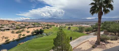 A view of a golf course with a palm tree, a river, and mountains in the background.