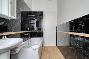 Ein modernes Badezimmer mit einer weißen Badewanne, einem Holzbadezimmermöbel und schwarzen Marmorfliesen.